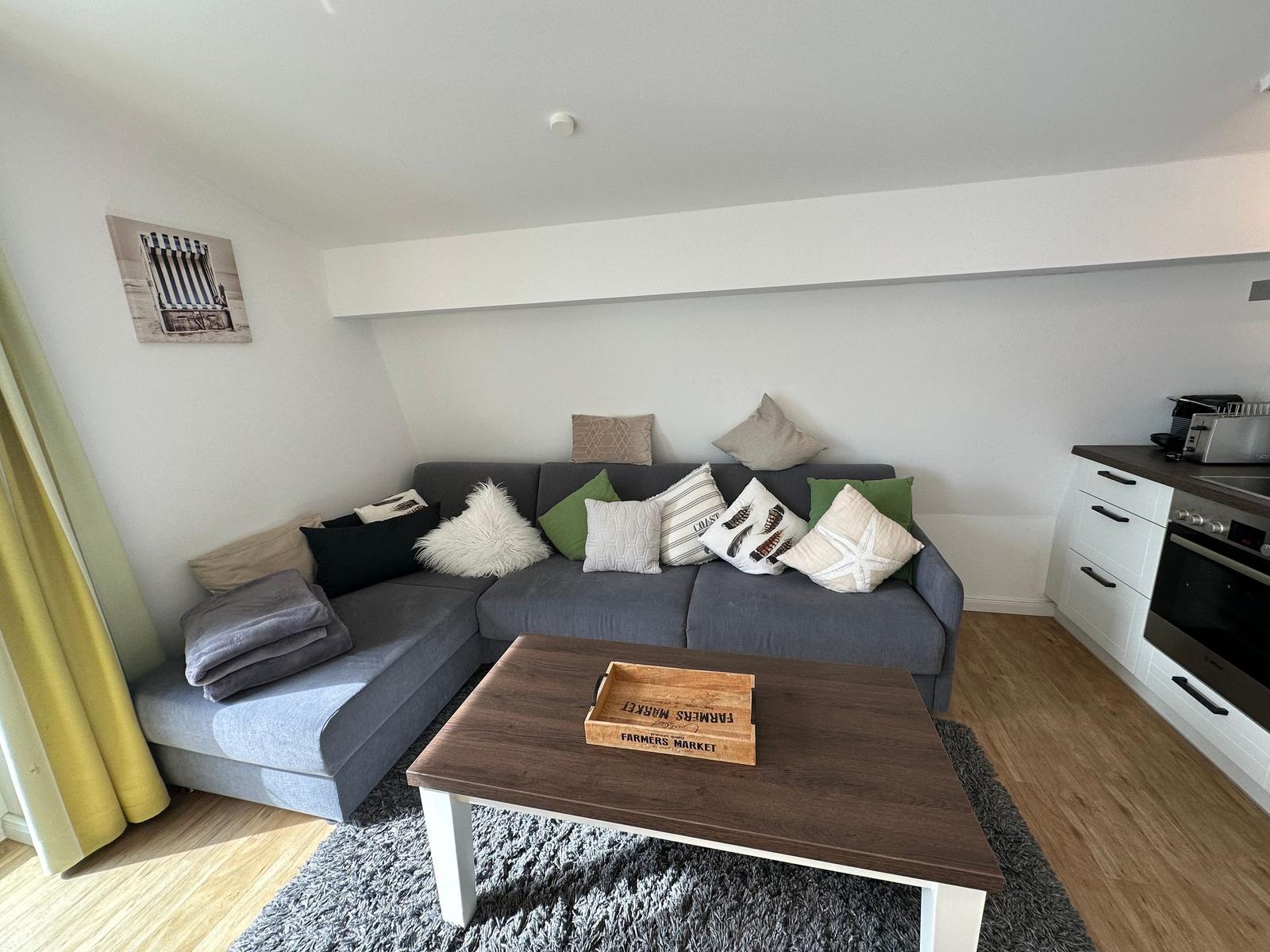 Ein Wohnzimmer mit grauem Sofa, Holztisch und Küchenbereich.