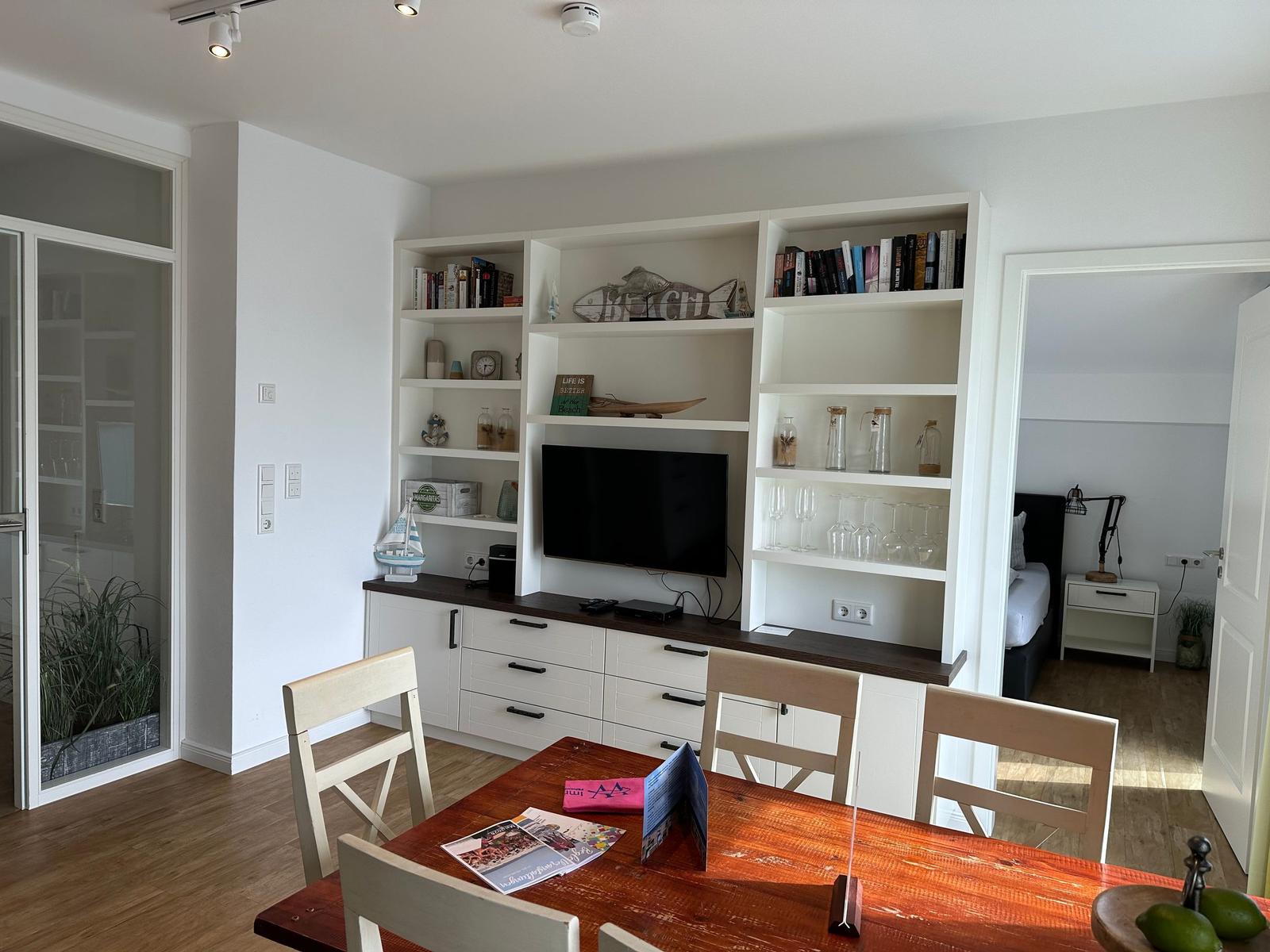 Wohnbereich mit Essbereich, Bücherregal und TV. Schlafzimmer ist sichtbar.