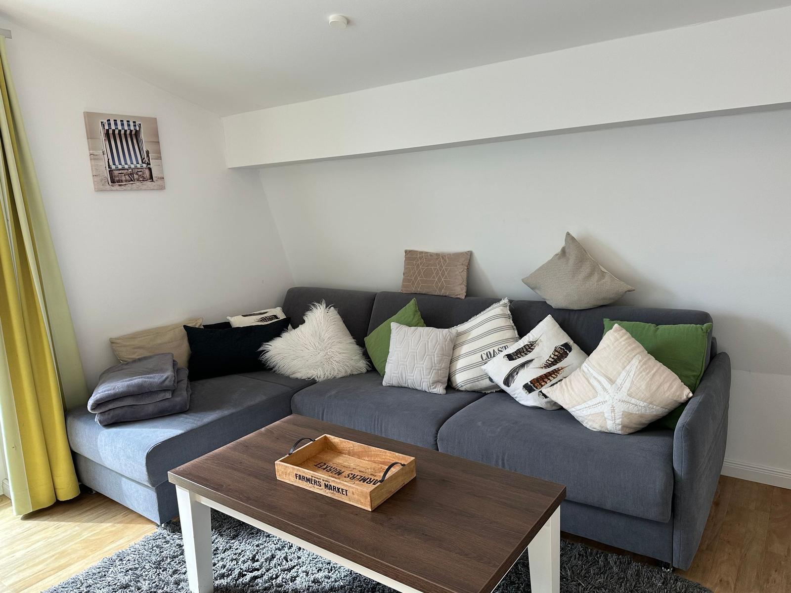 Ein Wohnzimmer mit grauem Sofa, Kissen und Holztisch.