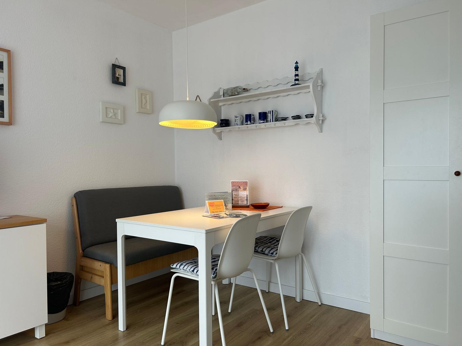Esstisch mit zwei Stühlen und Bänkchen an der Wand. Hängeschrank und Lampe darüber.