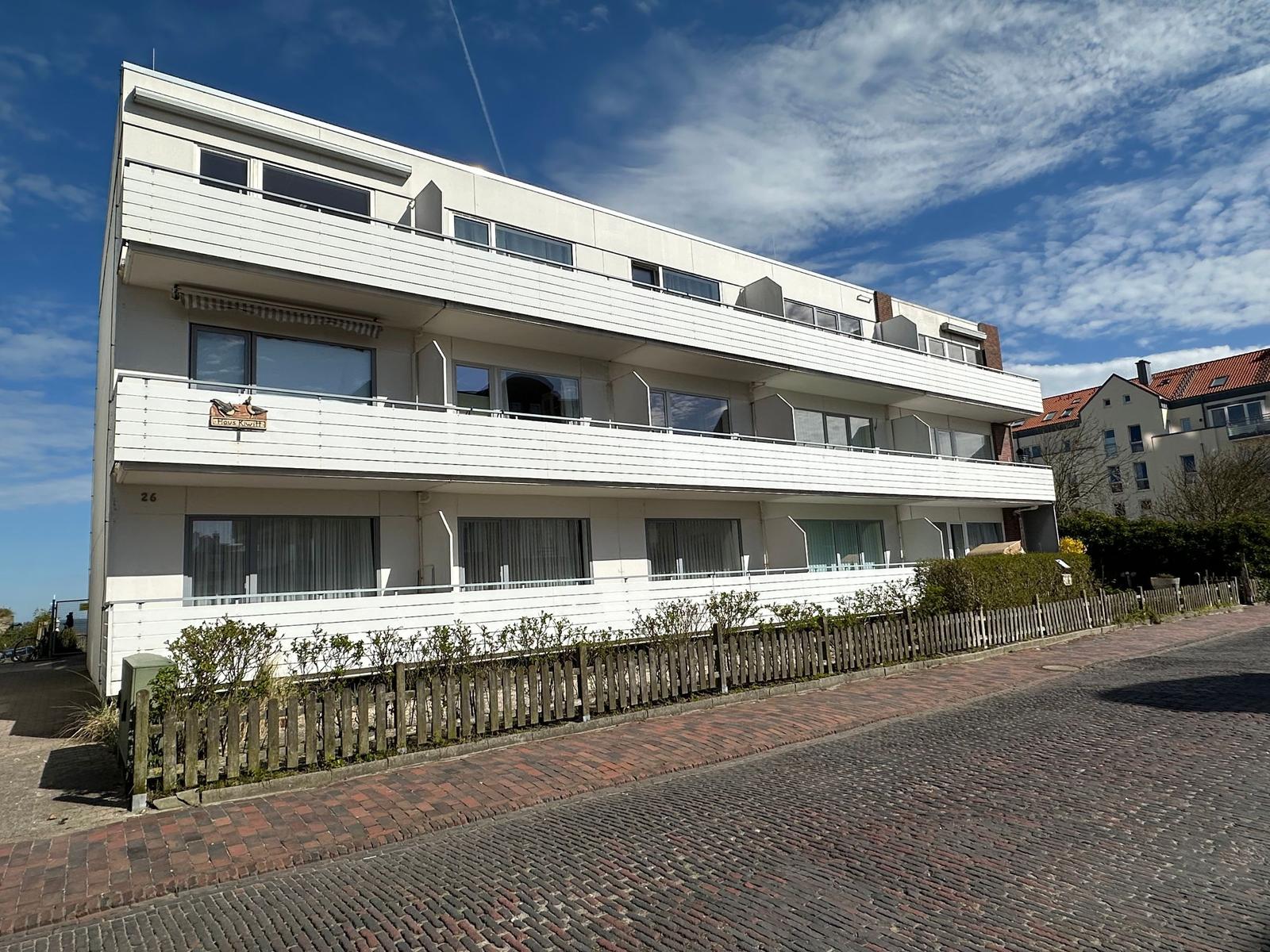 Modernes Mehrfamilienhaus mit Balkonen und Fenstern. Vor dem Haus befindet sich ein Holzzaun.