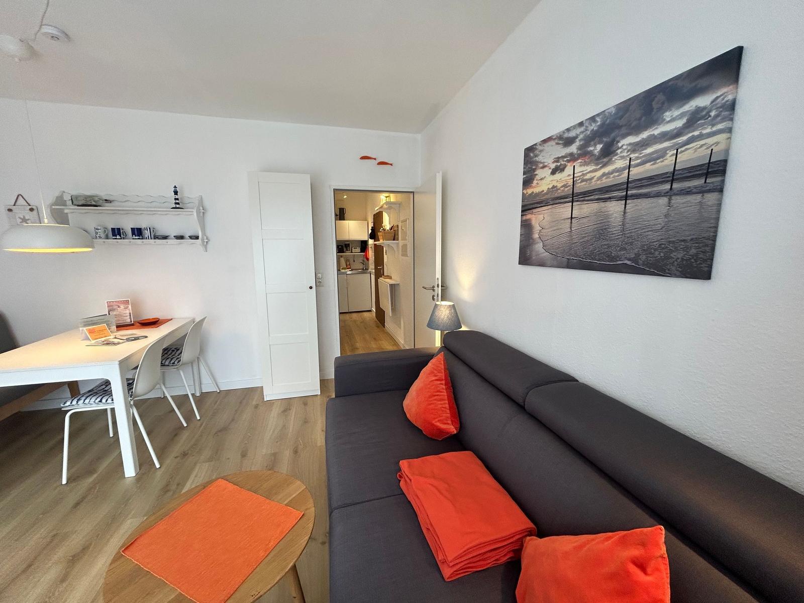 Wohnzimmer mit Sofa, Tisch und Küchenbereich im Hintergrund.