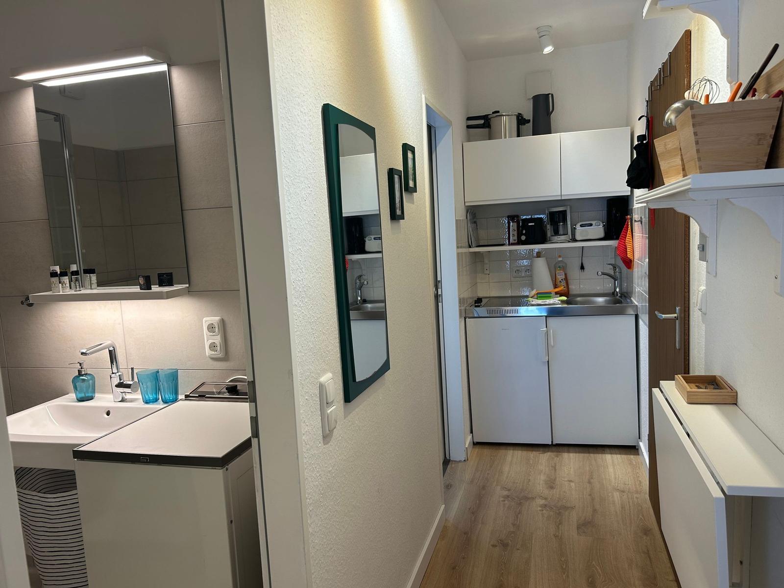 Küche mit Spüle, Kühlschrank und Aufbewahrung. Badezimmer mit Waschbecken und Spiegel.