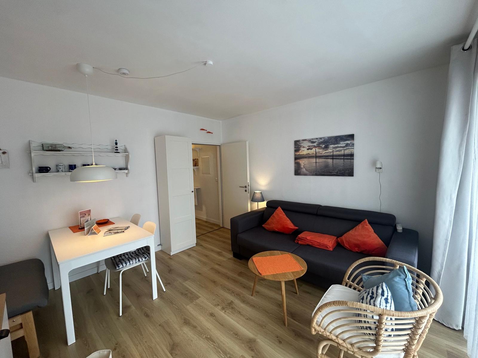 Wohnzimmer mit Sofa, Esstisch und Wandbild. Holzdielenboden und weiße Wände.