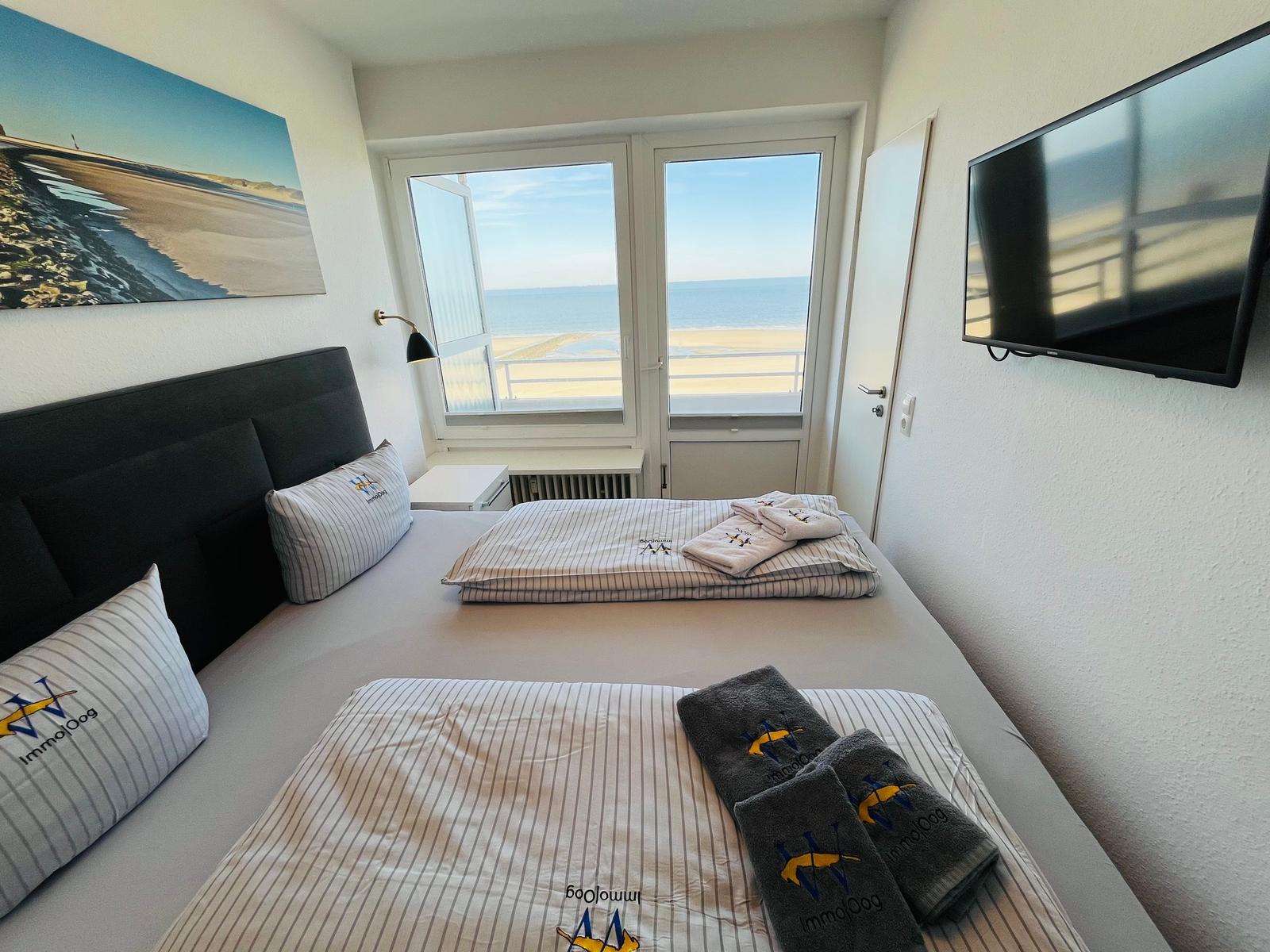Schlafzimmer mit Blick aufs Meer, Bett mit Bettwäsche und TV.