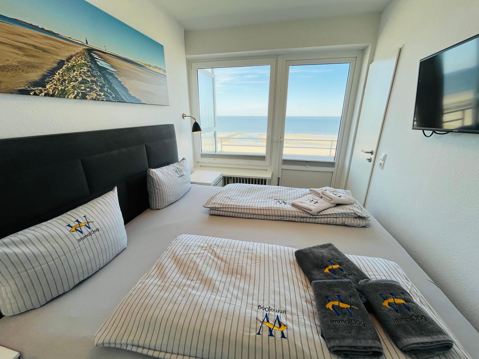 Schlafzimmer mit Blick aufs Meer und TV. Bett mit Handtüchern und Kissen.