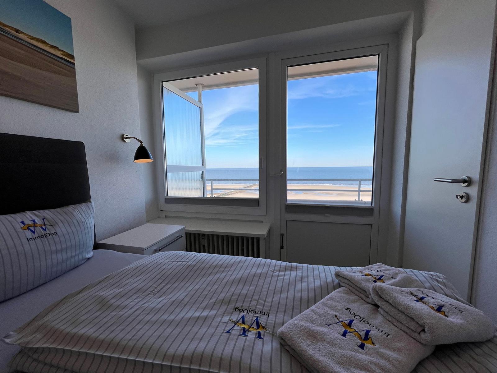 Schlafzimmer mit Blick auf Strand und Meer. Bett mit Bettwäsche und Handtüchern.