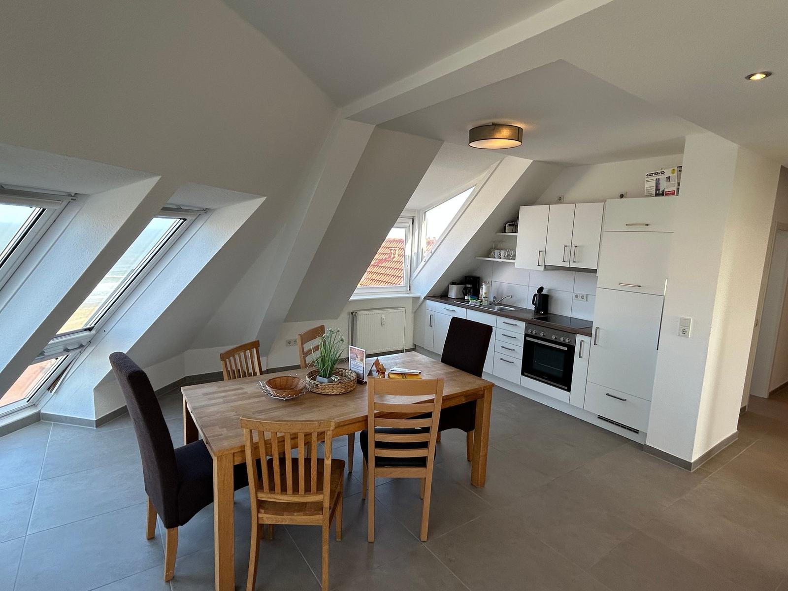 Essbereich mit Tisch und Stühlen unter Dachschrägen. Küche mit weißen Schränken und Fenster.