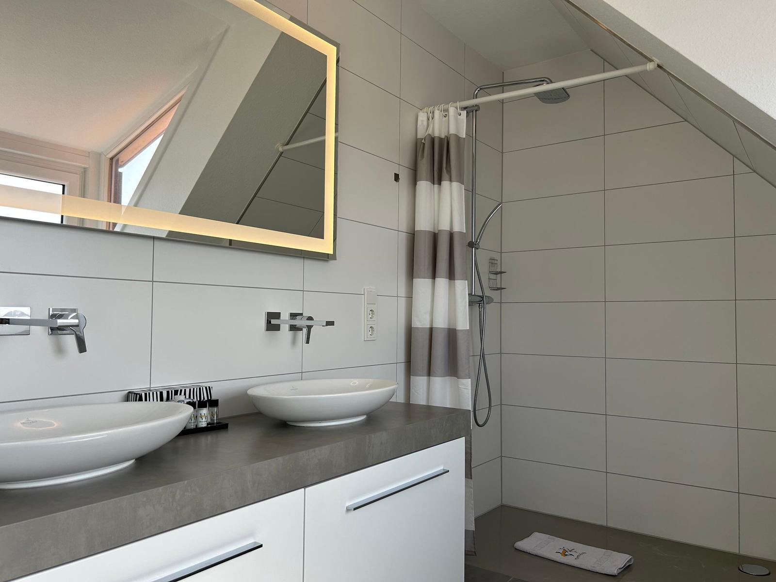 Badezimmer mit Dusche, Waschbecken und beleuchtetem Spiegel