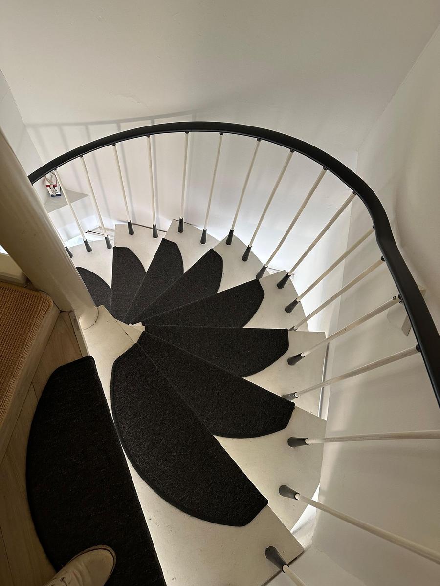 Spiralförmige Treppe mit schwarzem Teppich und weißem Geländer.