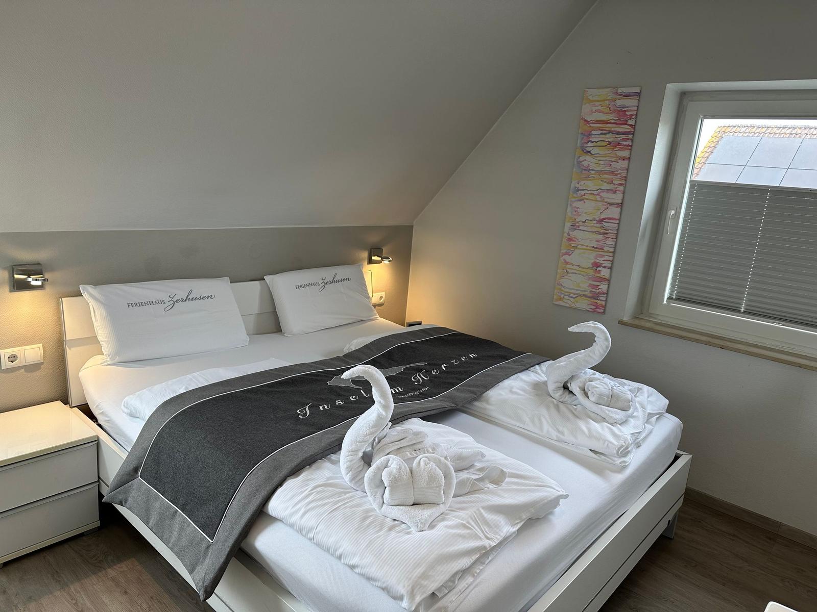 Schlafzimmer mit Doppelbett, Fenster und Kissen mit Hotellogo.