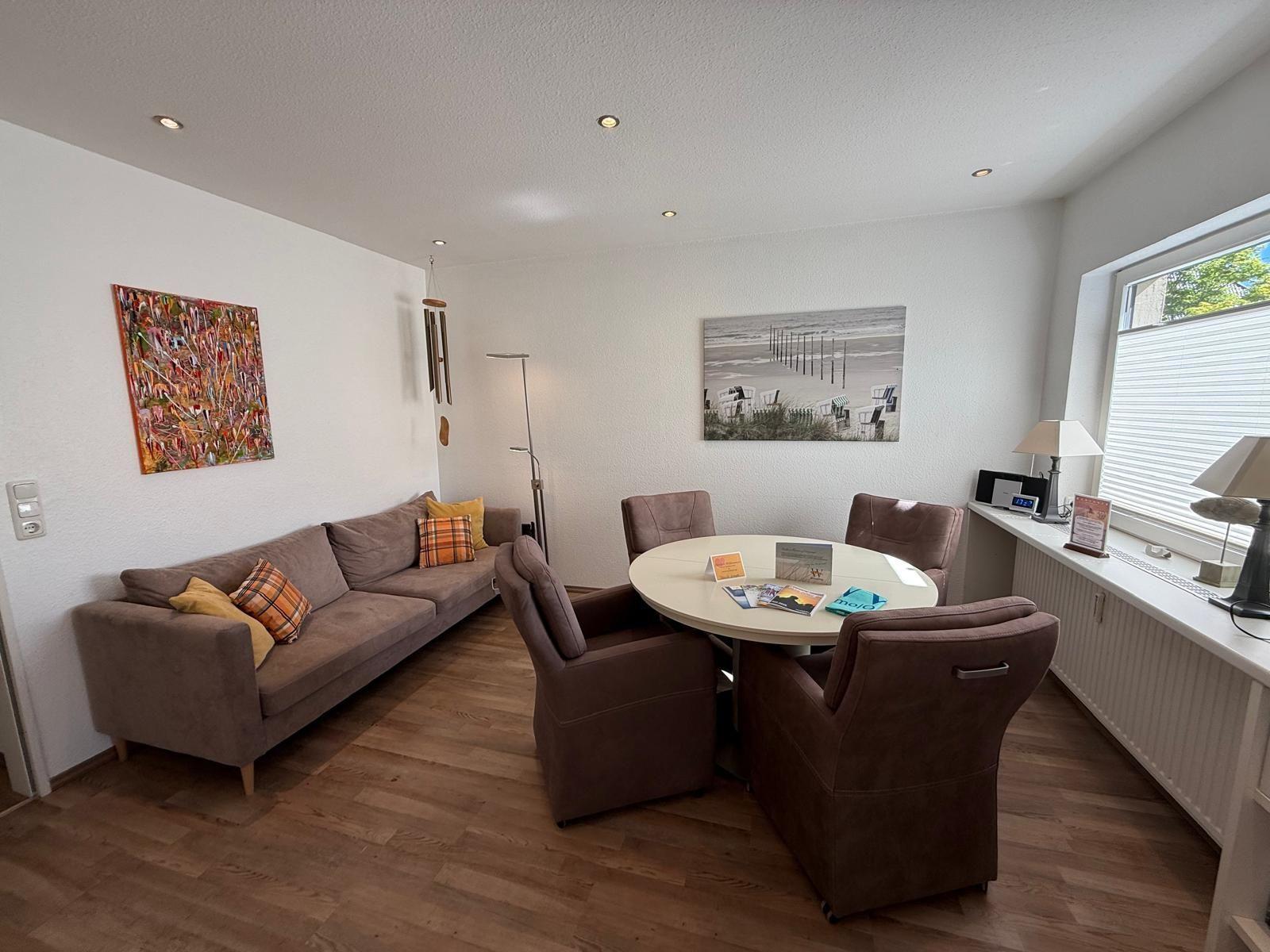 Wohn- und Essbereich mit Sofa, runden Tisch und Stühlen, Wandbildern und Holzboden.