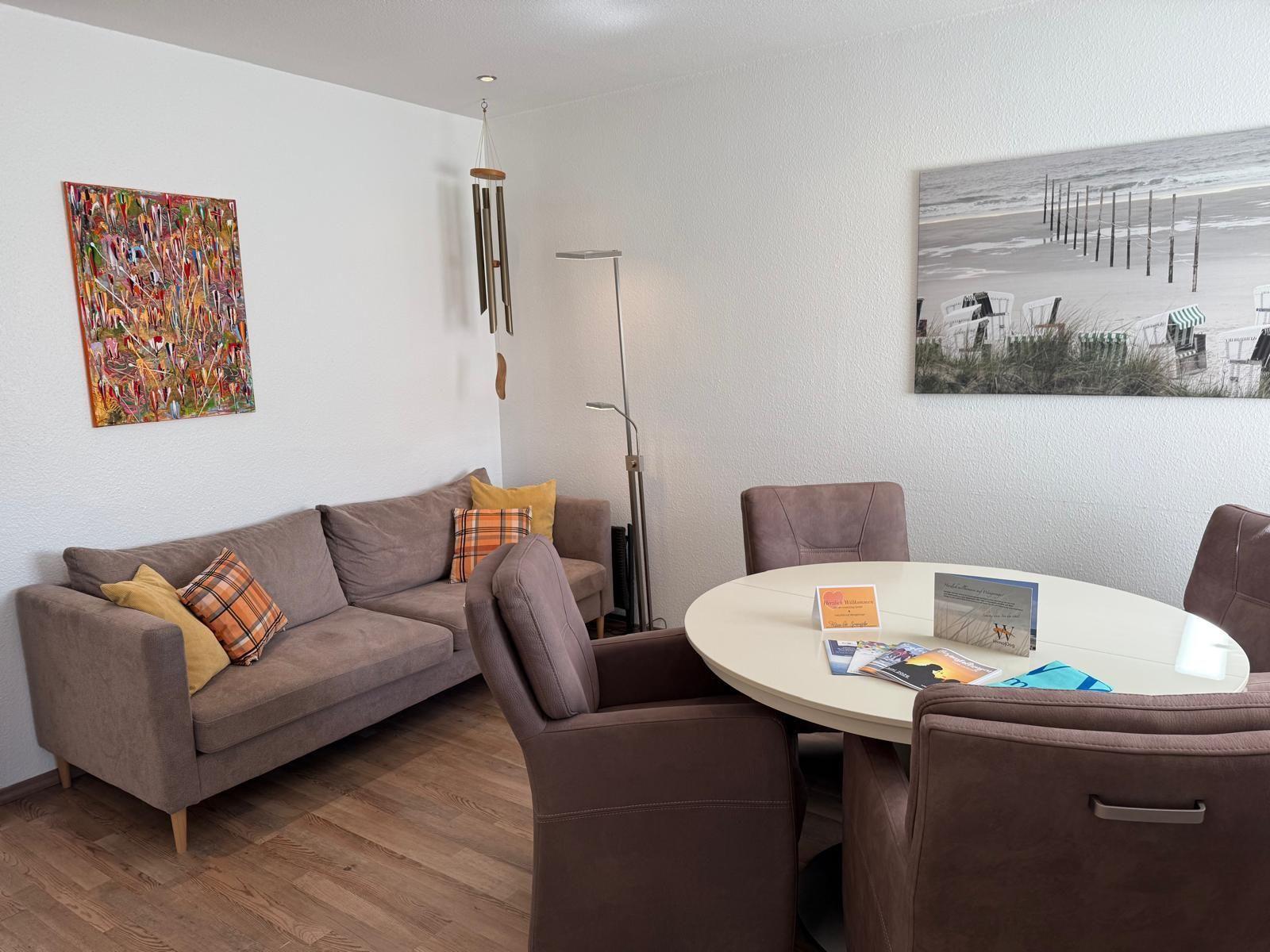 Wohn- und Essbereich mit Sofa, runden Tisch und Wandbildern.