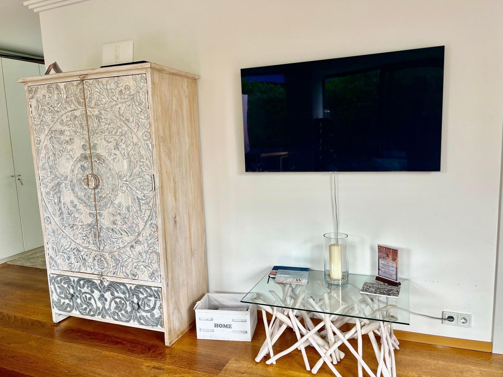 Wohnzimmer mit Fernseher, Glas-Tisch und kunstvollen Schränken.
