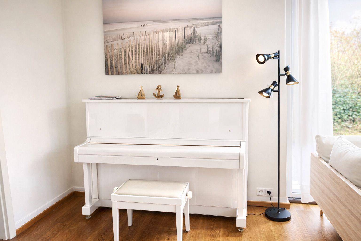 Weißes Flügelklavier mit Hocker, Wandbild und Stehlampe im Raum.