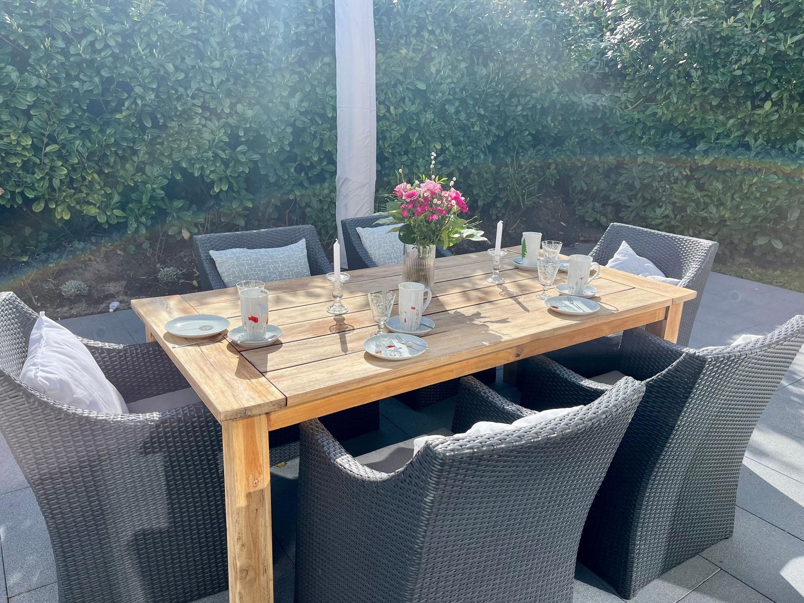 Holztisch mit sechs Stühlen, Blumen und Geschirr im Garten.
