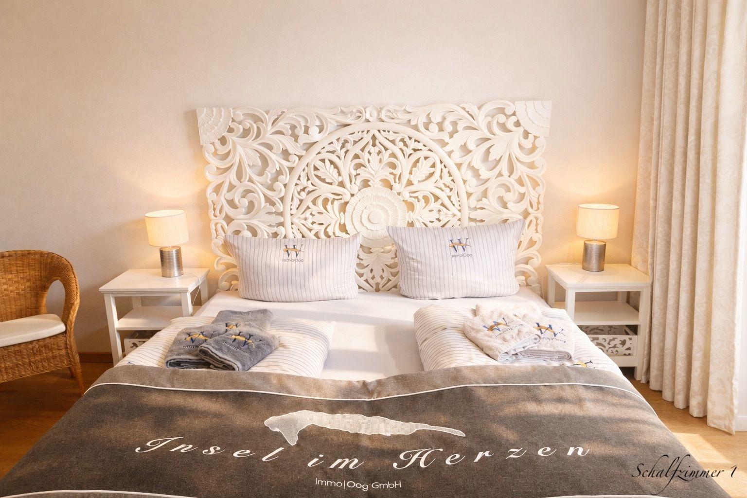 Schlafzimmer mit großem Bett, kunstvoller Kopfteil, zwei Nachttischen und Stuhl.
