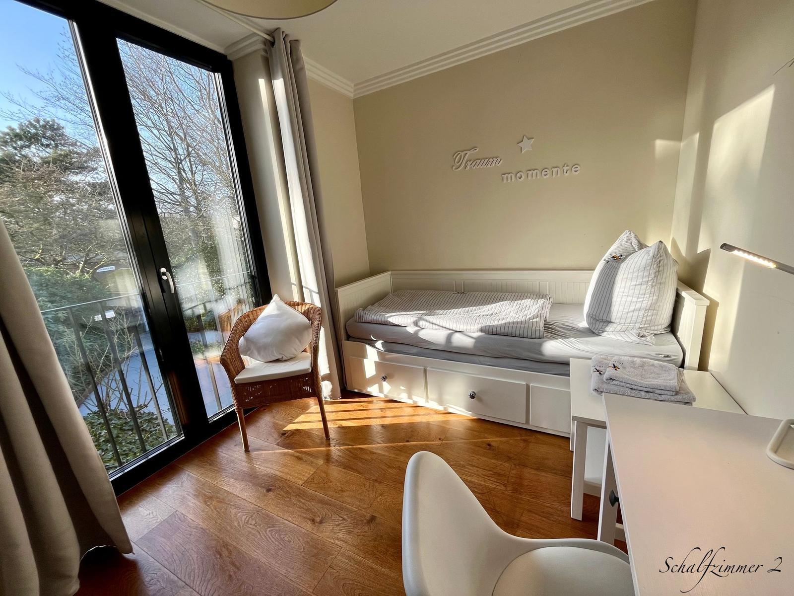 Schlafzimmer mit Bett, Schreibtisch und Balkontür. Wanddekoration mit Schriftzug.