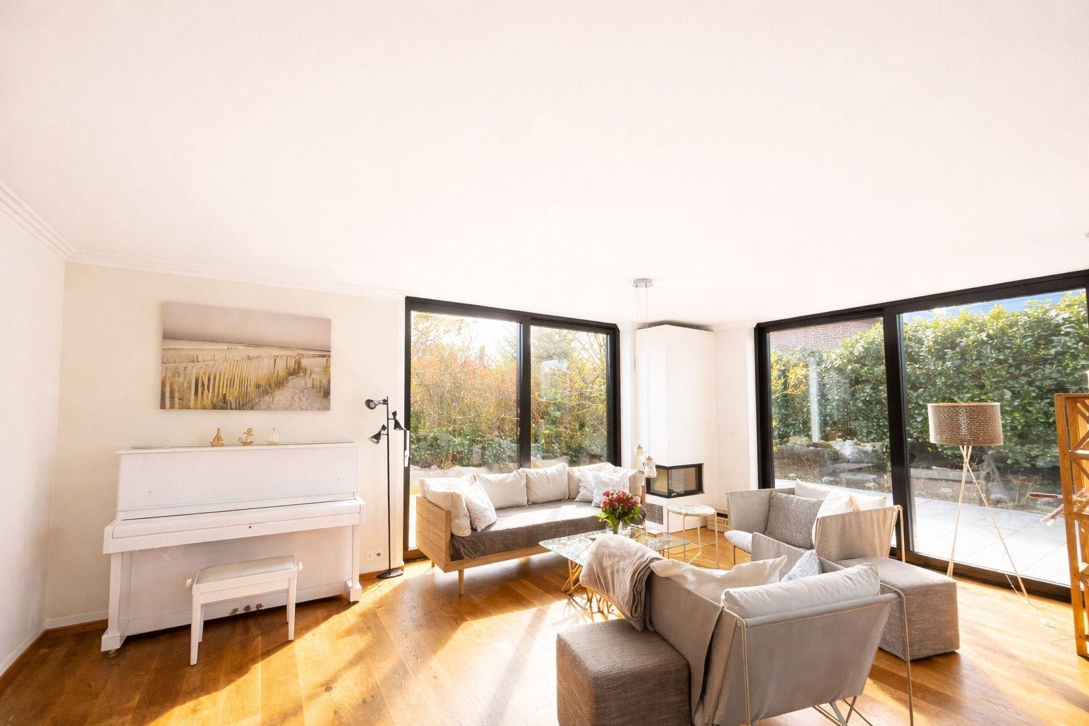 Wohnzimmer mit Klavier, Sofa und großen Fenstern zur Terrasse.
