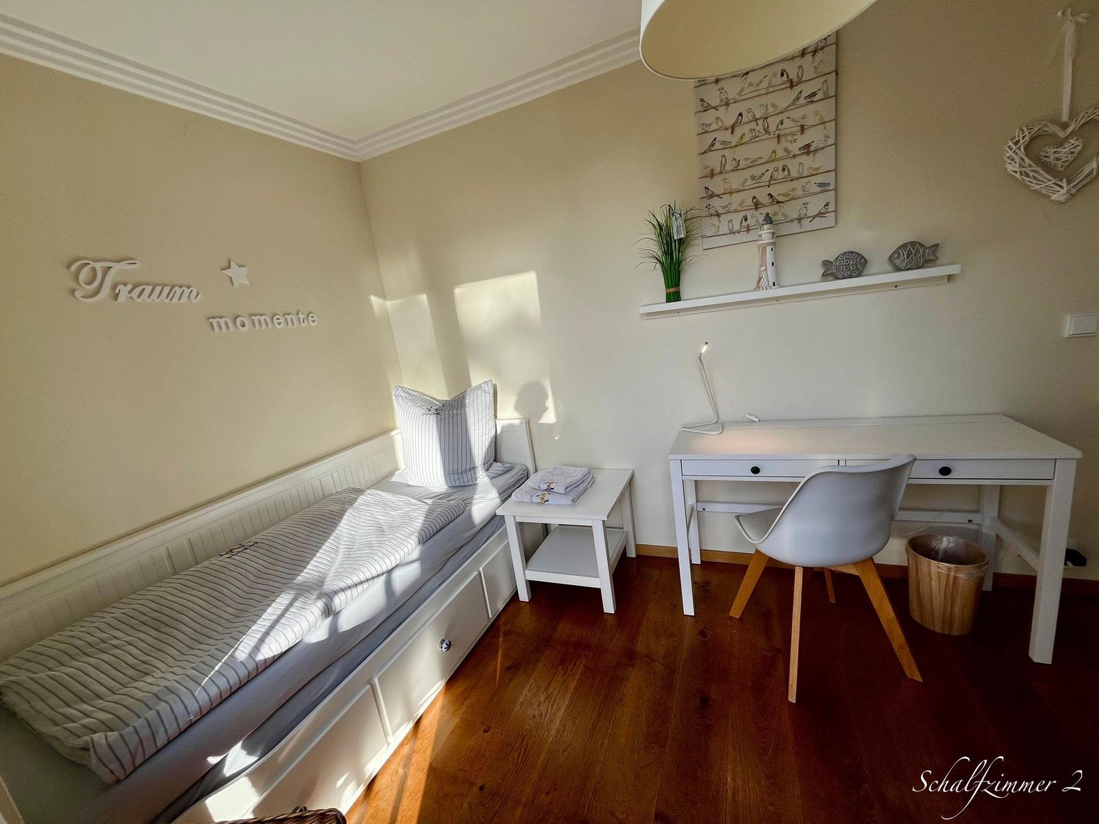 Schlafzimmer mit Bett, Schreibtisch und Wanddekoration.