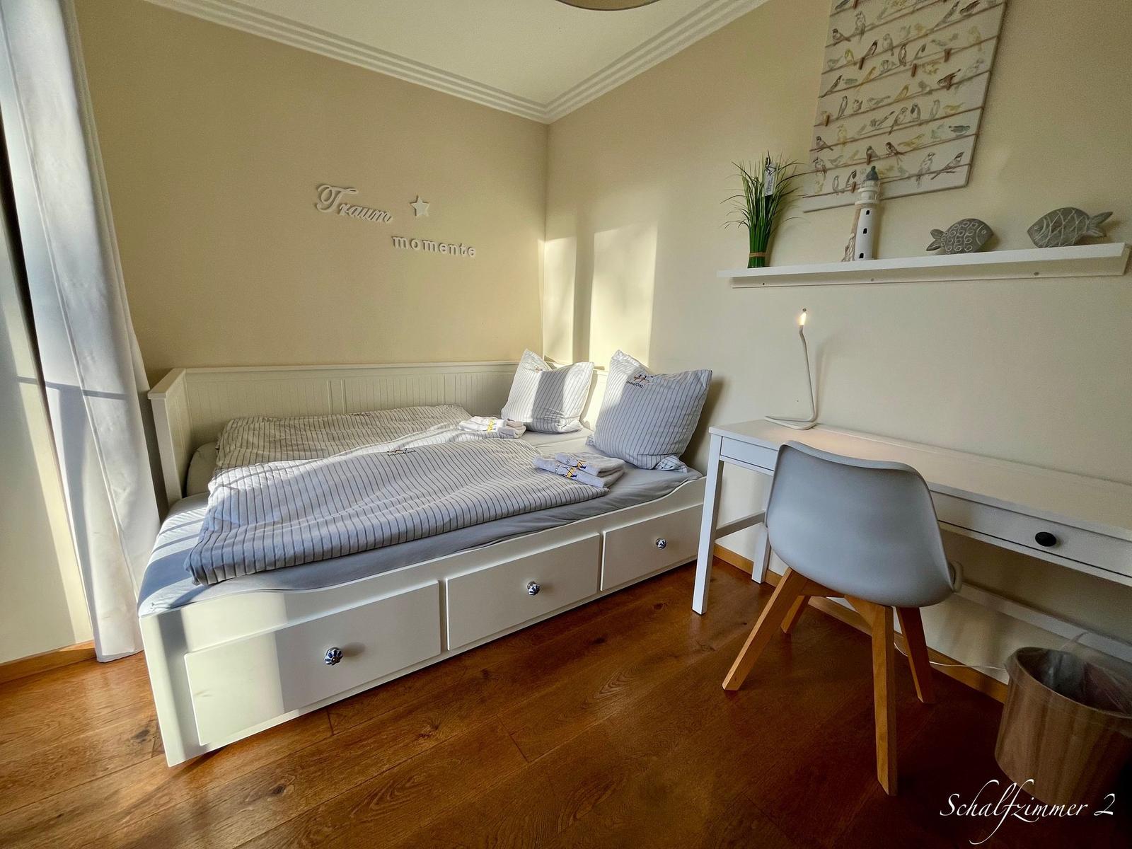 Schlafzimmer mit Bett, Schreibtisch und Wanddekoration.