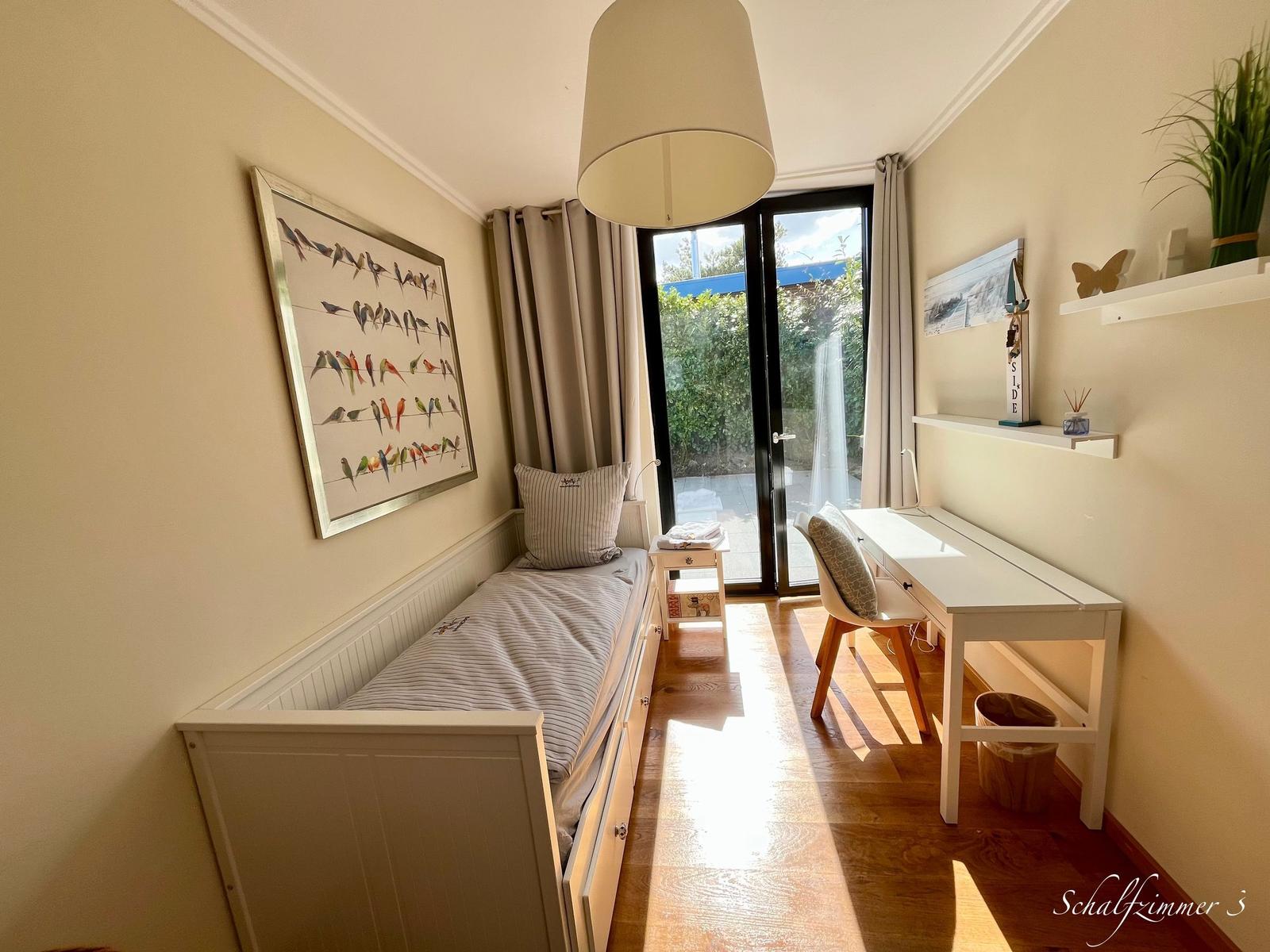 Schlafzimmer mit Bett, Schreibtisch und Fenster zur Terrasse.