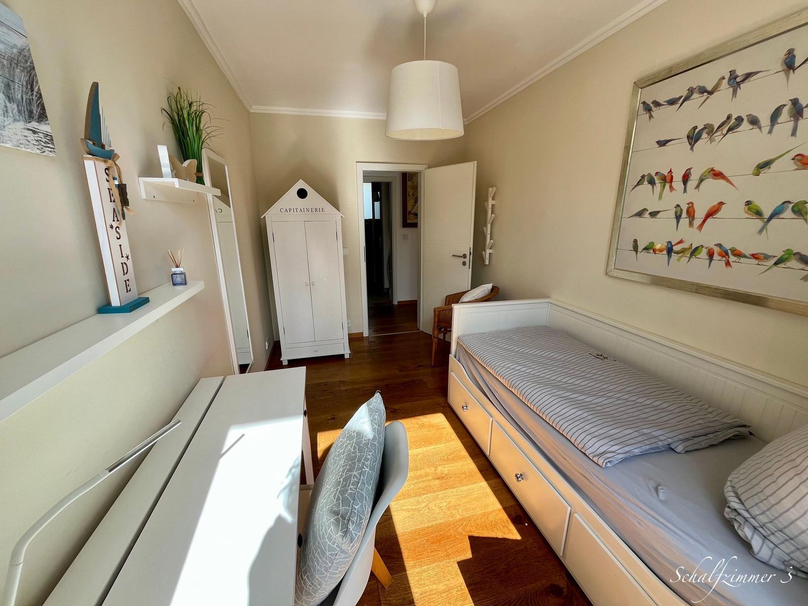 Schlafzimmer mit Bett, Schreibtisch und Kleiderschrank. Wandbild mit Vögeln und Holzboden.