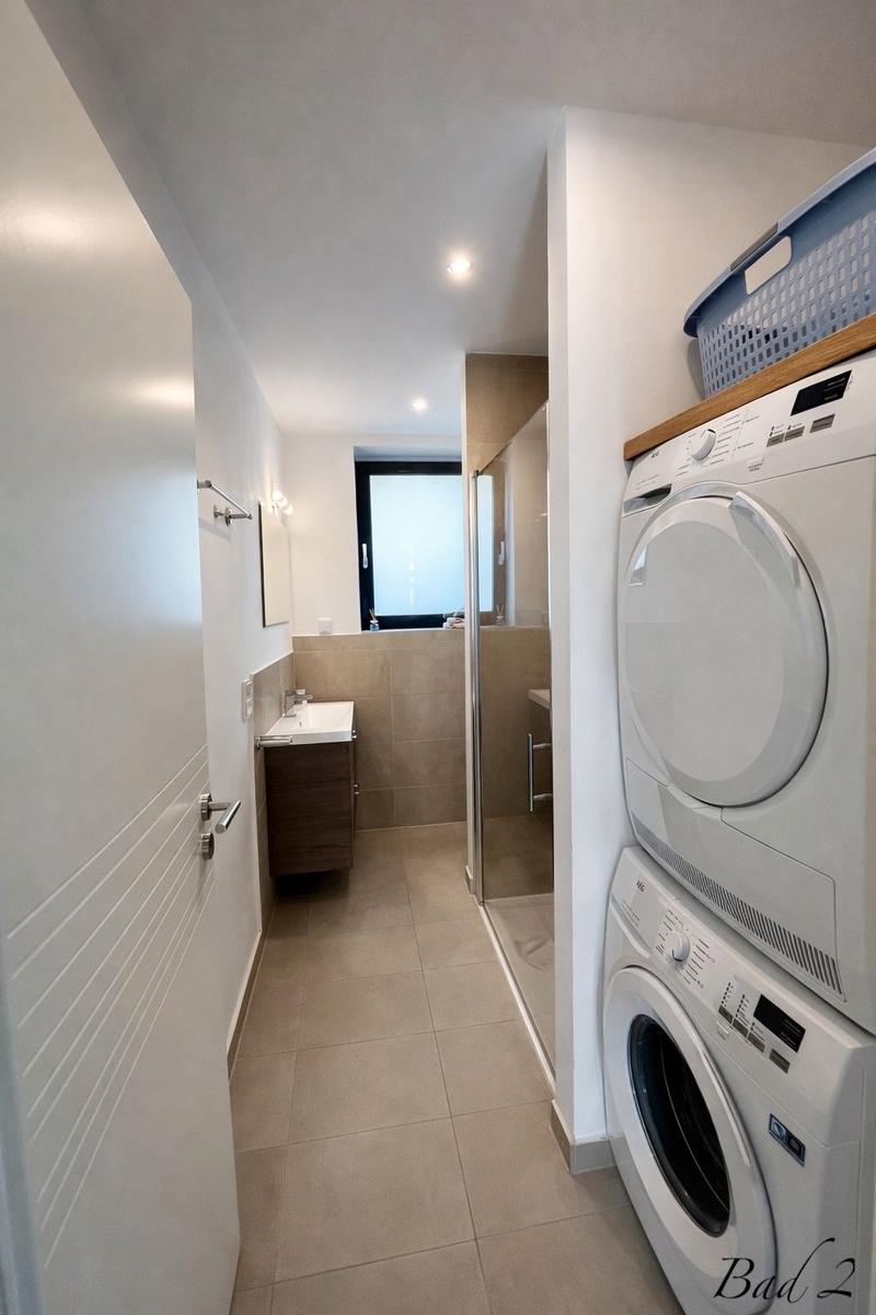 Wasch- und Trockneranlage neben Bad mit Waschbecken und Dusche.