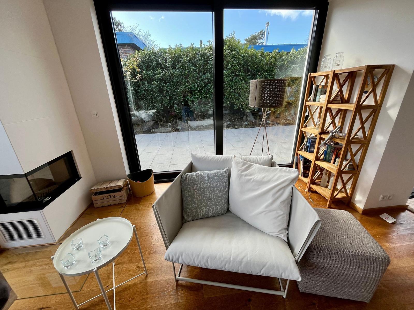 Sofa mit Kissen vor großem Fenster. Holzboden, Bücherregal und Kamin.