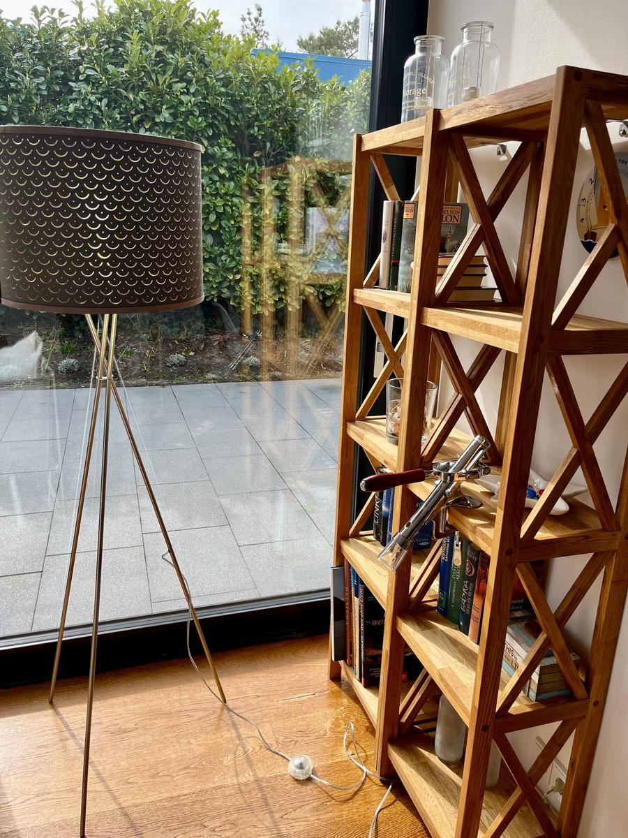 Helle Ecke mit Holzregal, Stehlampe und Blick auf Terrasse.