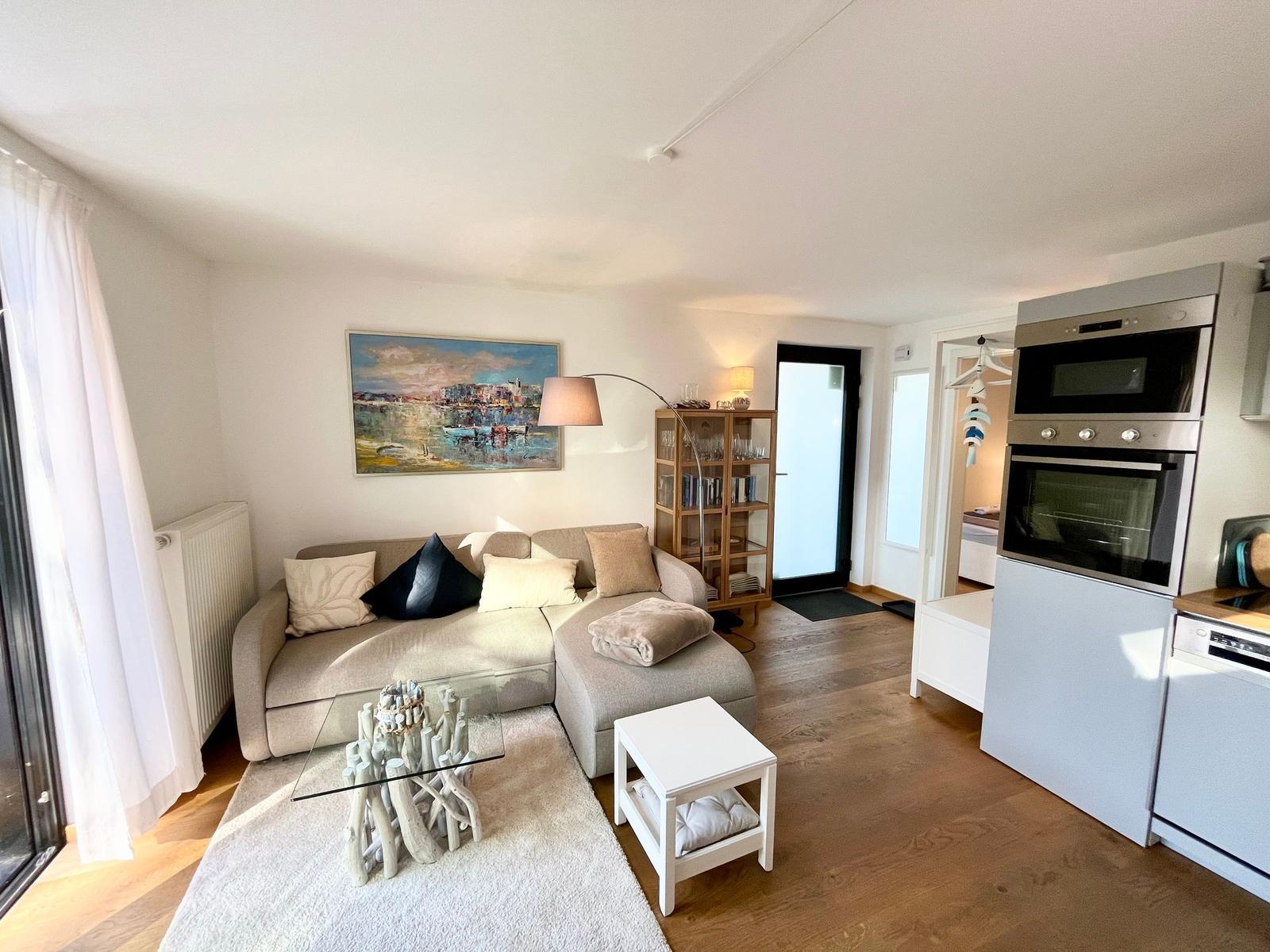 Wohnzimmer mit Sofa, Glas-Tisch und Küchenzeile
