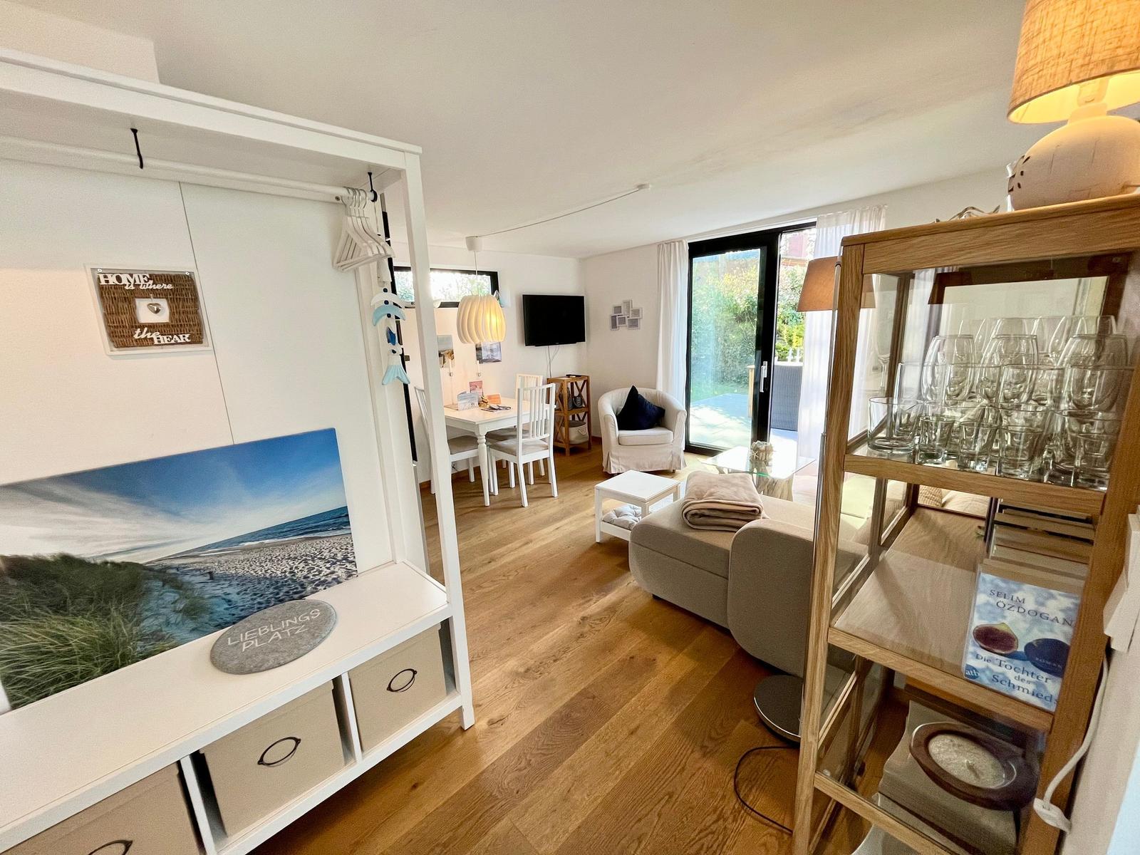 Wohnzimmer mit Essbereich, Glasfront und Holzboden. Regal mit Gläsern und Bildern.