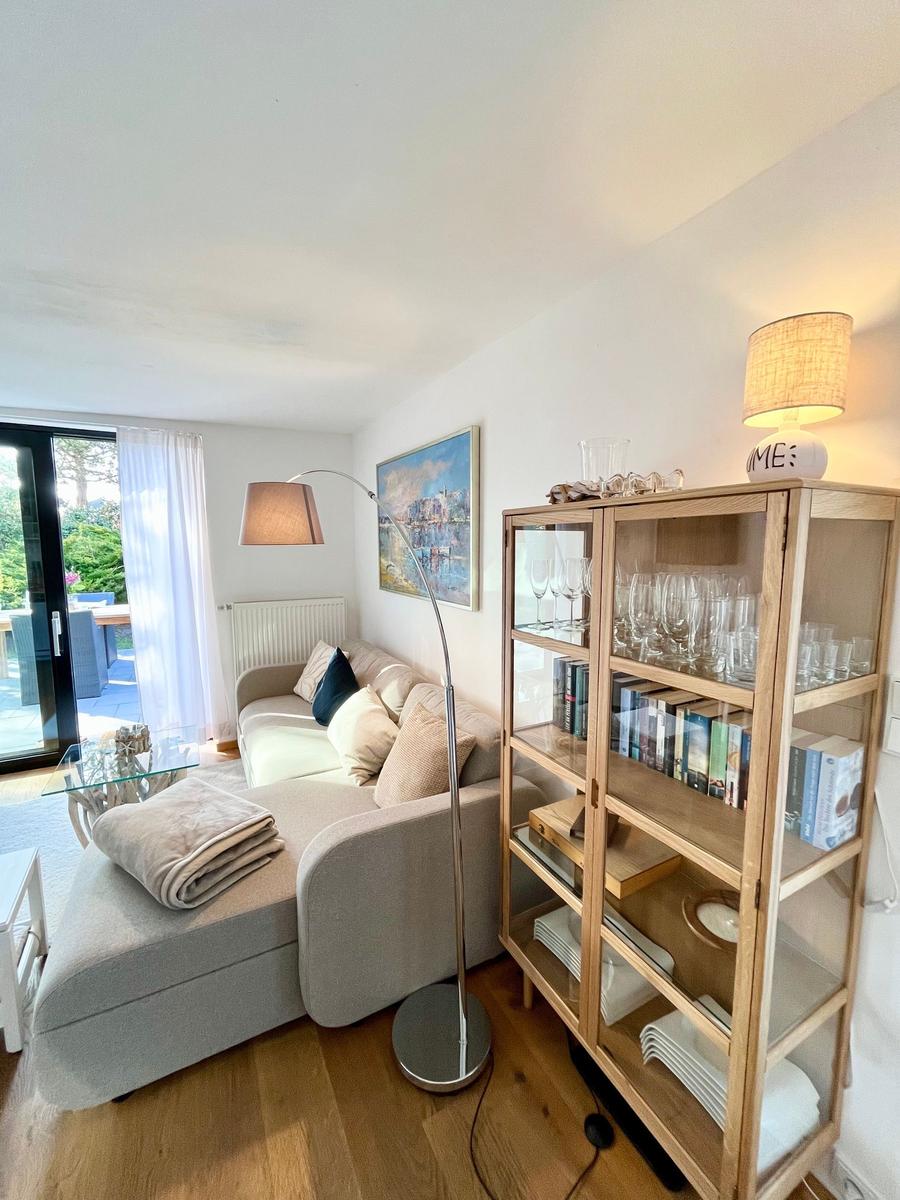 Wohnzimmer mit Sofa, Glasregal und Terrassentür.