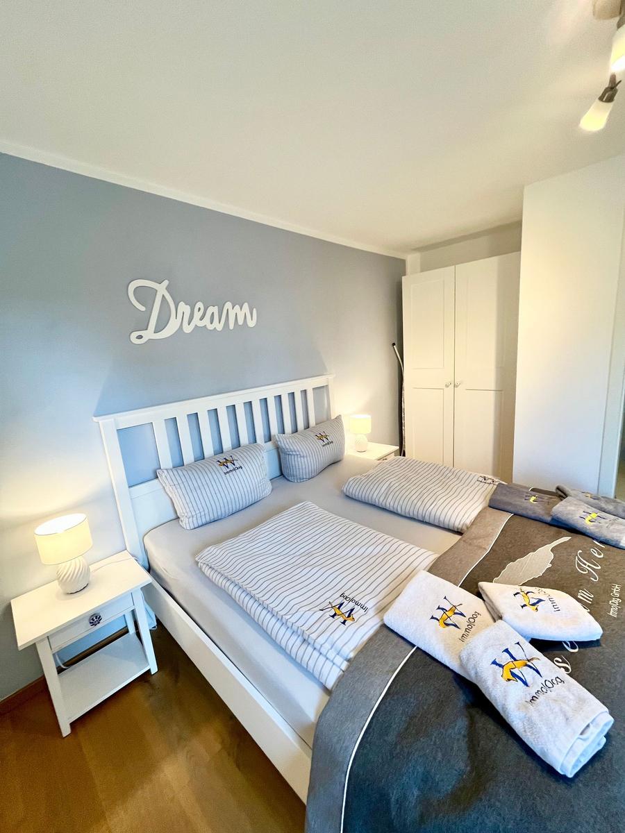 Schlafzimmer mit Doppelbett, Nachttisch und Kleiderschrank. Wanddekoration mit Dream.