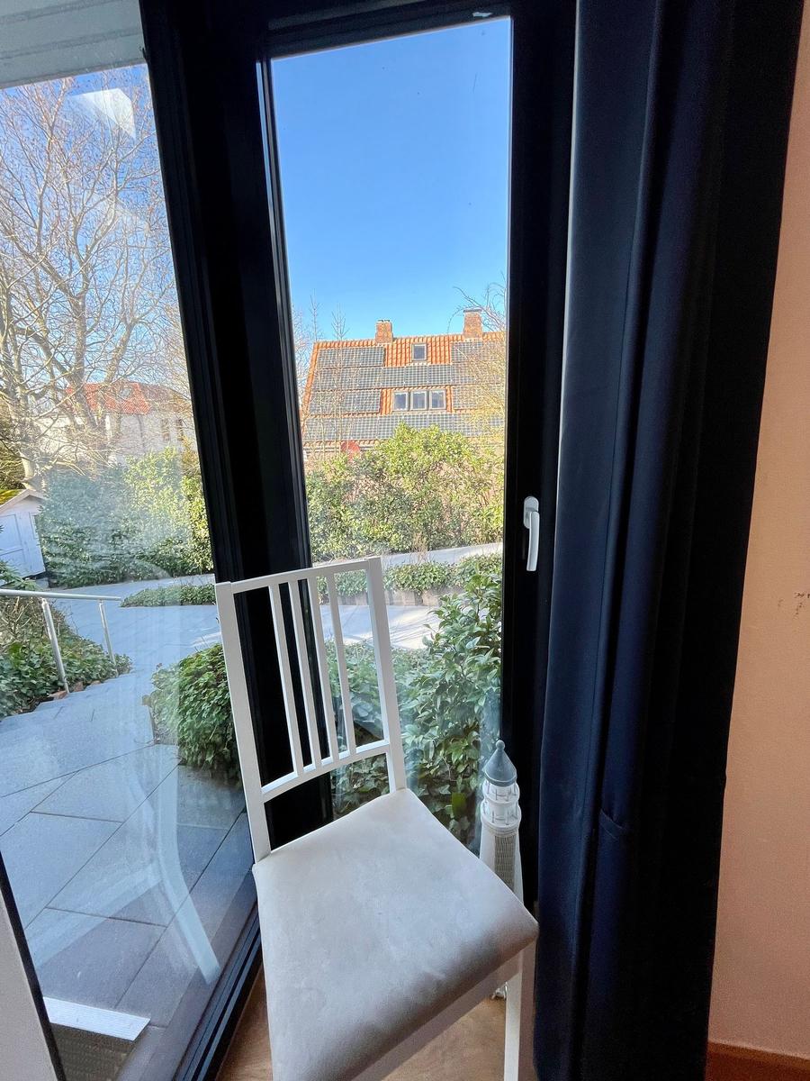 Weißer Stuhl vor Fenster mit Blick auf Garten und Dach