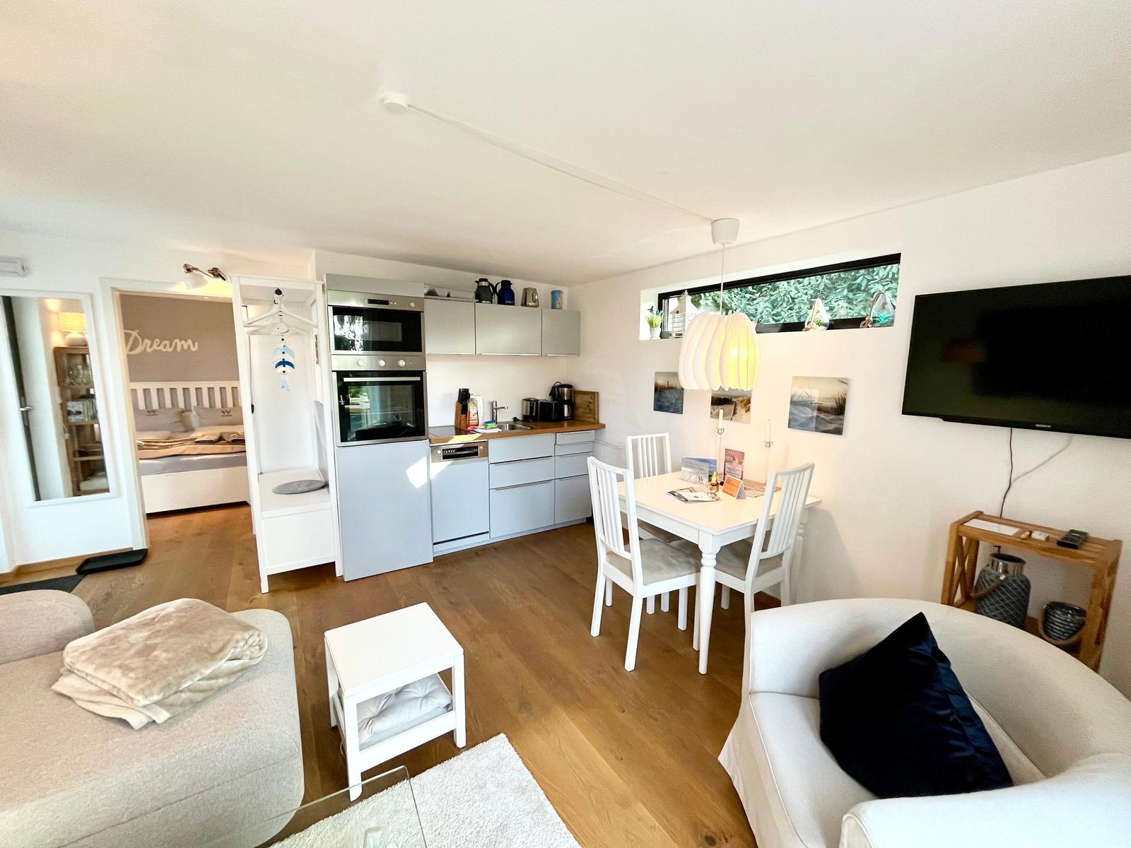 Wohnbereich mit Küche, Esstisch und Schlafzimmer im Hintergrund.