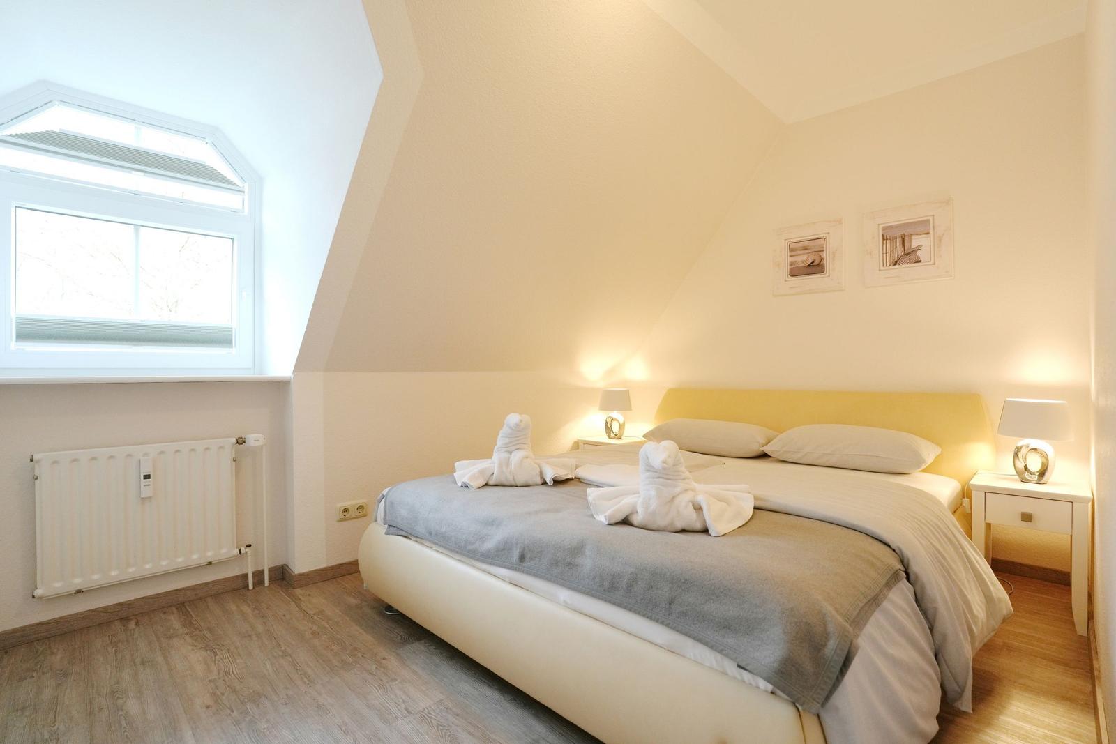 Schlafzimmer mit Dachschräge, Bett mit Handtuchfiguren und Fenster.