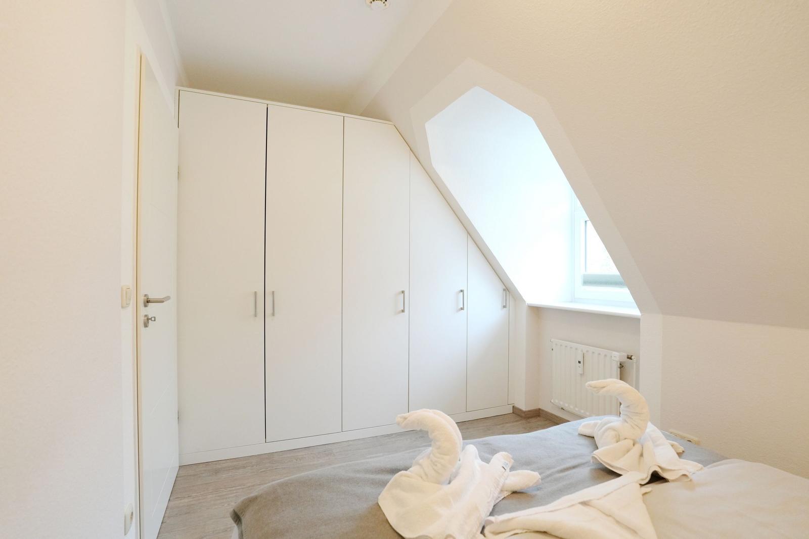 Schlafzimmer mit Dachschrägen, weißer Kleiderschrank und Bett mit Handtüchern