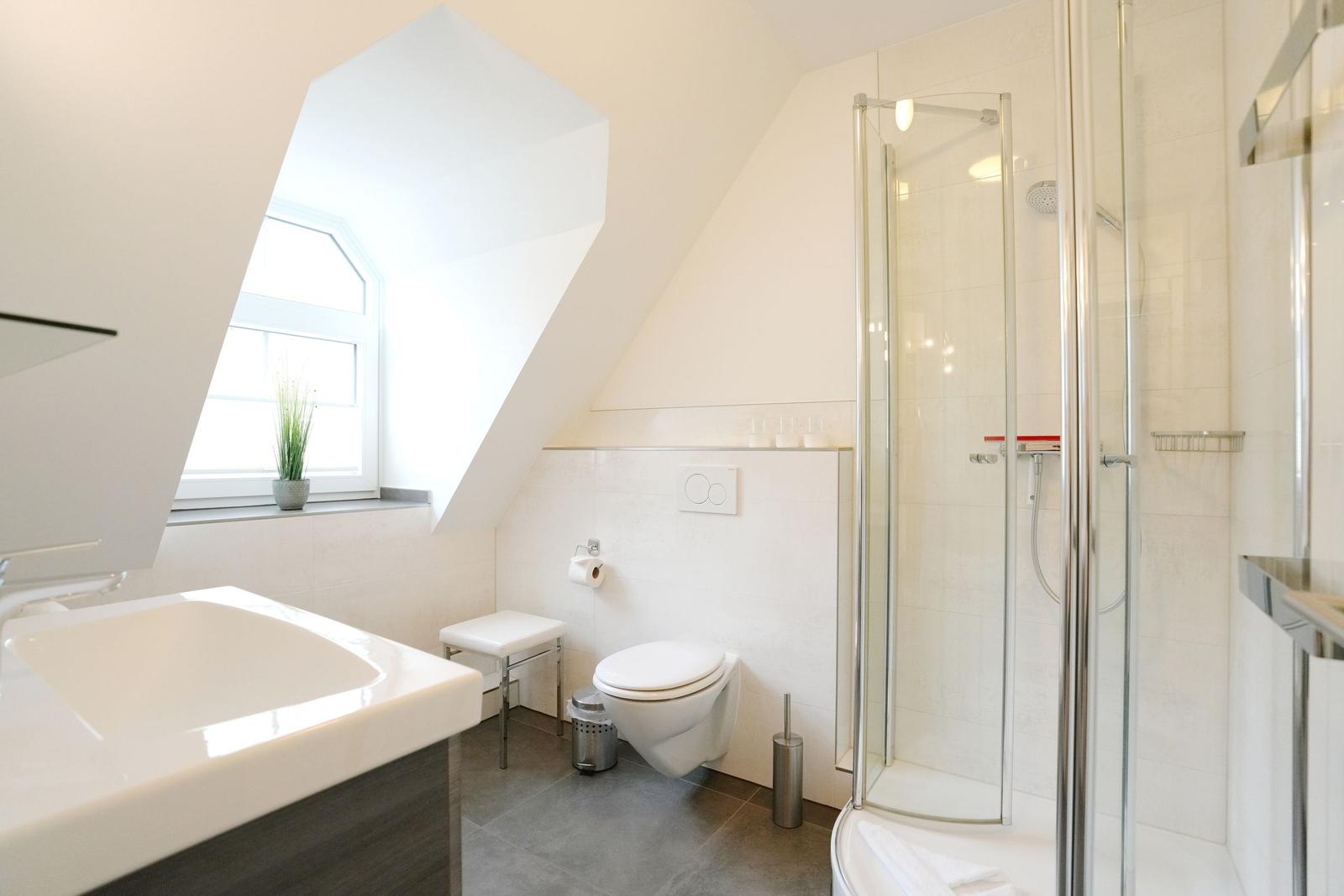 Badezimmer mit Dusche, WC und Waschbecken unter Dachschräge mit Fenster.