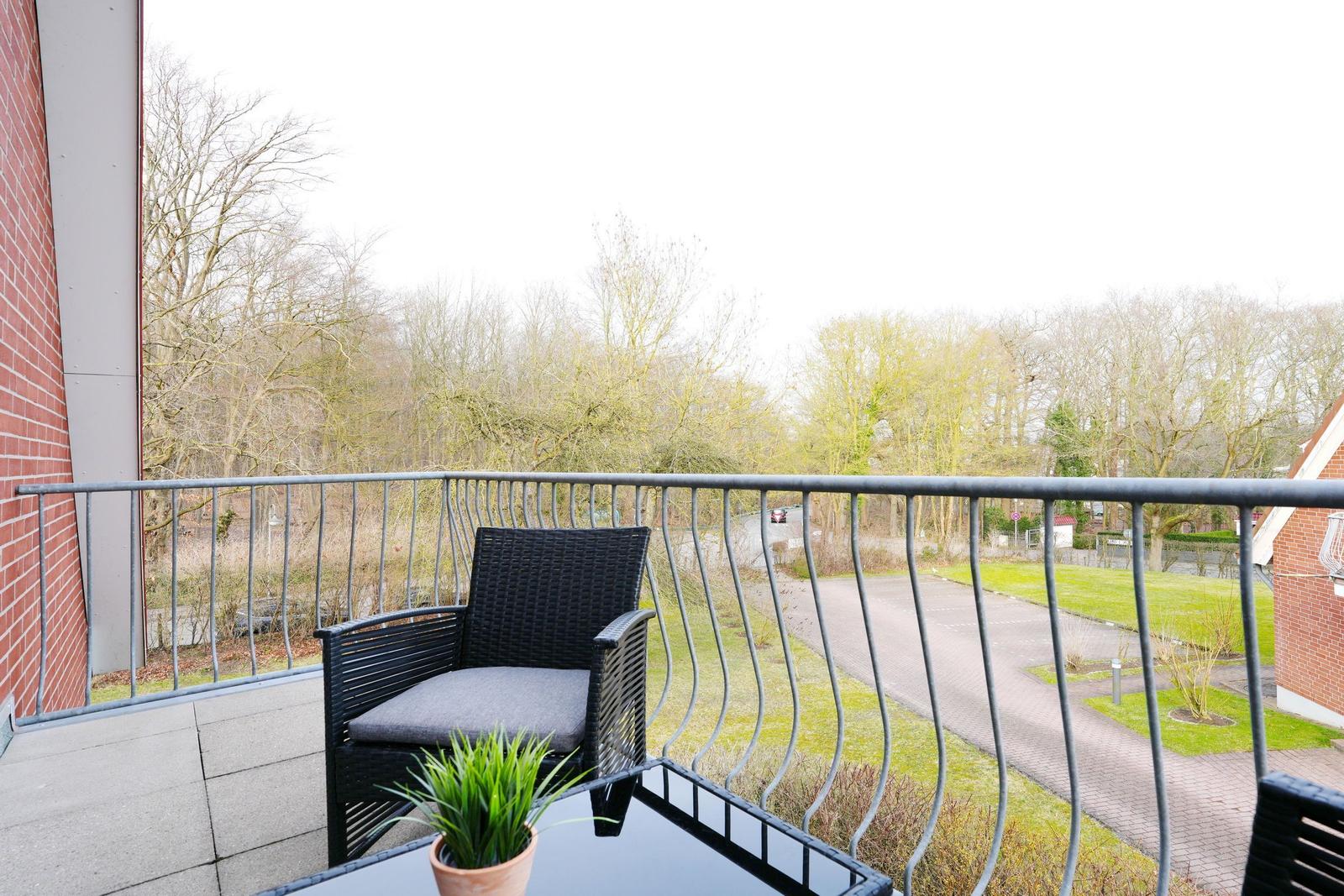 Balcony with black wicker chair and small potted plant overlooking trees and pathway.