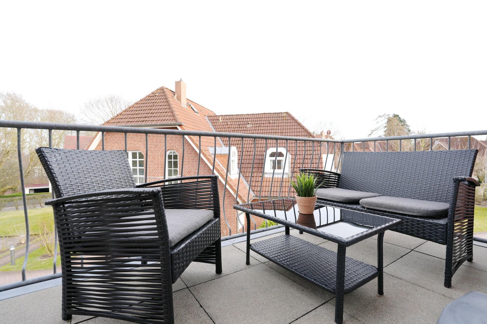 Terrasse mit Sitzgruppe und Tisch. Blick auf rote Dächer und Grünflächen.