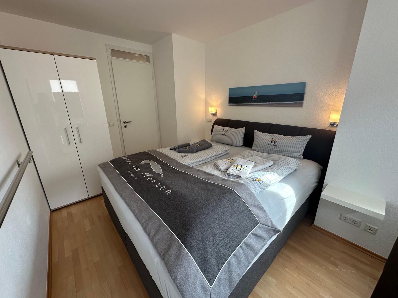 Schlafzimmer mit Doppelbett, Kleiderschrank und Wandbild mit Segelboot.