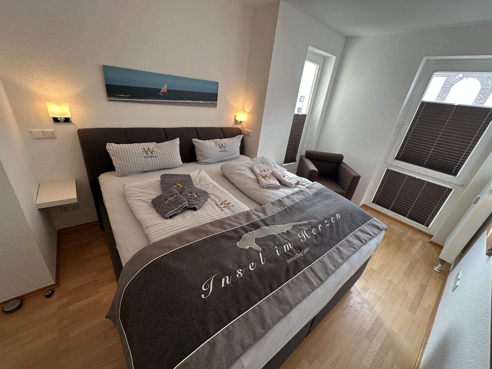 Schlafzimmer mit Doppelbett, Bettwäsche und Fenster mit Jalousien.