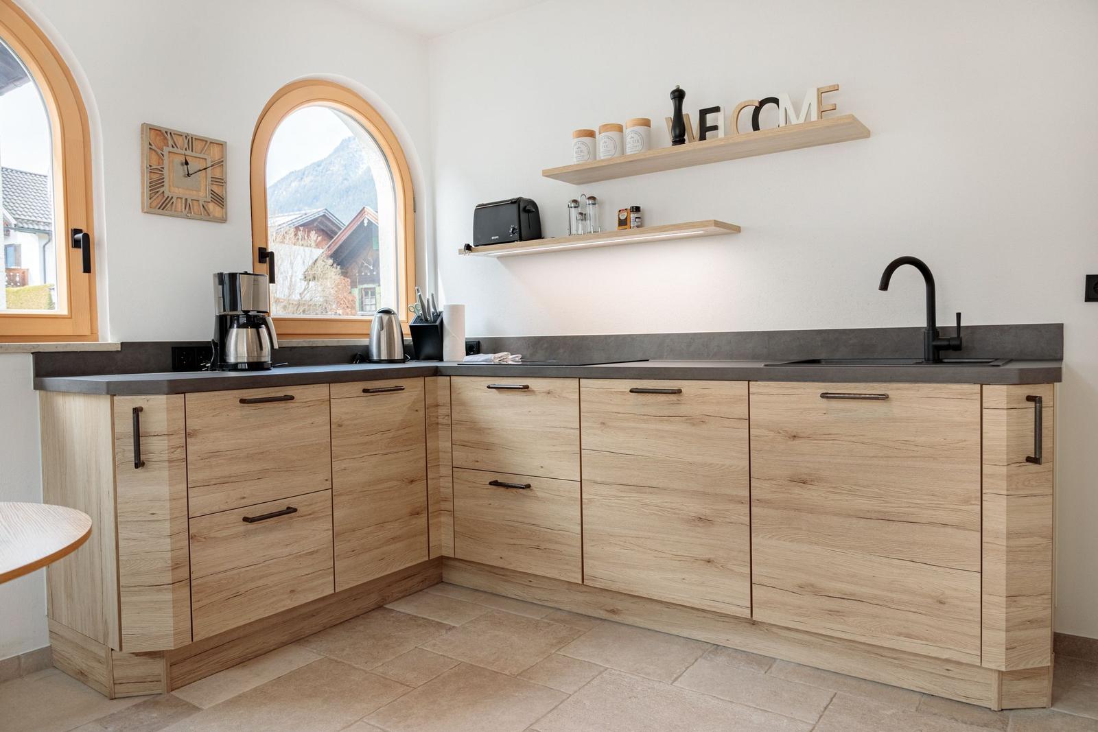 Küche mit Holzschränken, dunkler Arbeitsplatte und Bogenfenstern mit Bergblick.