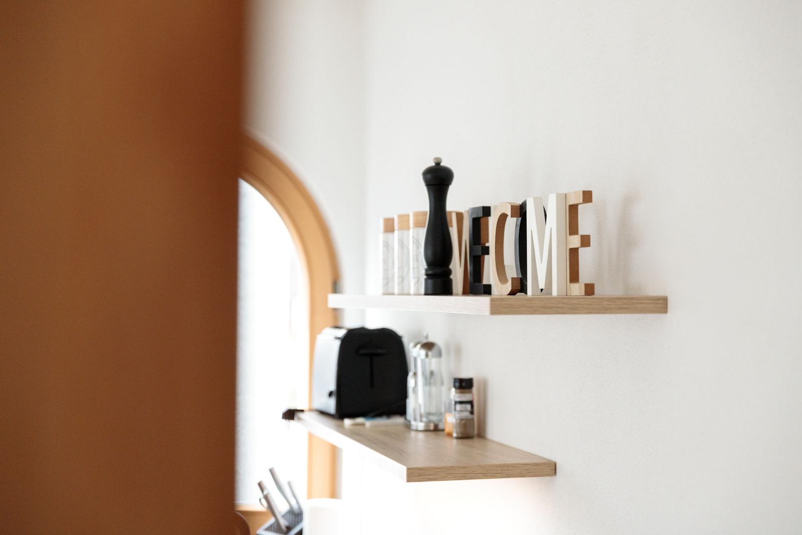 Wohnbereich mit Holzregal, Kaffeemaschine und WELCOME-Schild