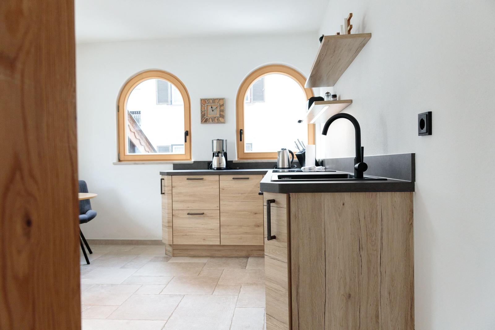 Küche mit Holzschränken, dunkler Arbeitsplatte und zwei Bogenfenstern.