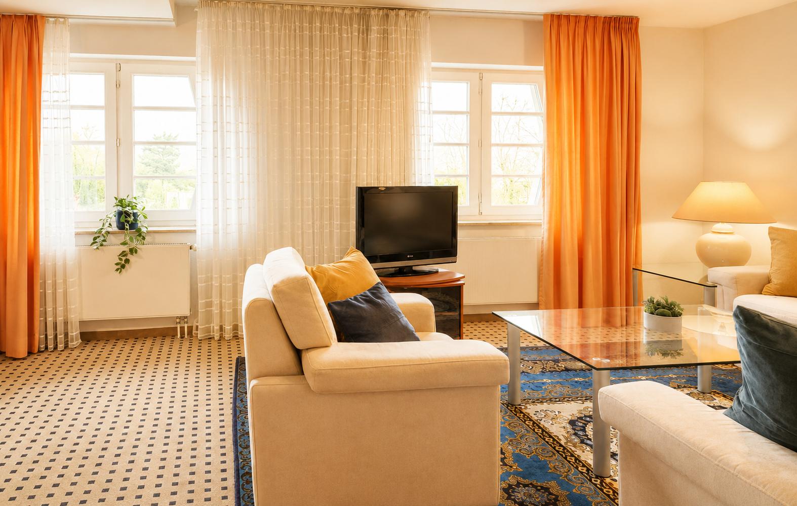 Wohnzimmer mit Sofa, Fernseher und Fenstern mit orangefarbenen Vorhängen.