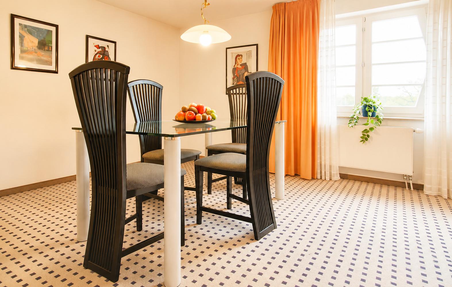 Esszimmer mit Glas-Tisch, vier Stühlen und orangefarbenen Vorhängen an Fenster.