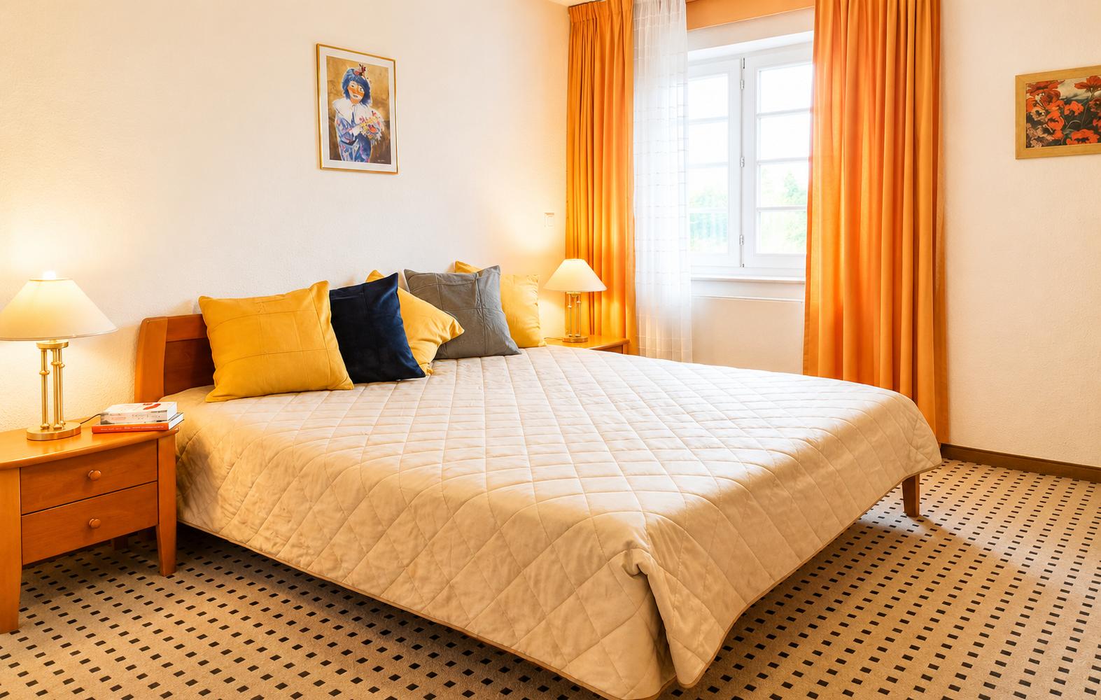 Schlafzimmer mit Bett, Nachttischen und Fenster mit orangefarbenen Vorhängen.