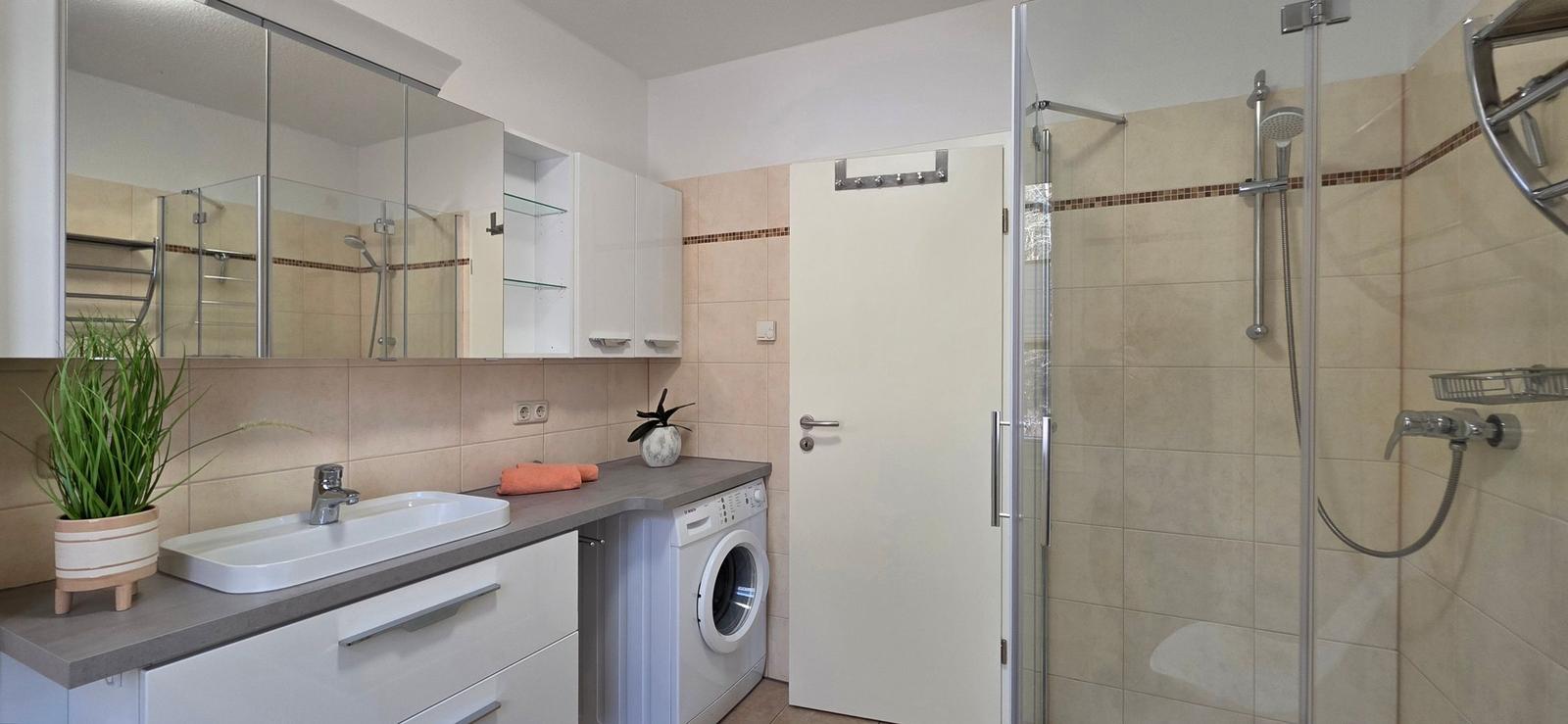 Badezimmer mit Dusche, Waschmaschine und Spiegelschrank
